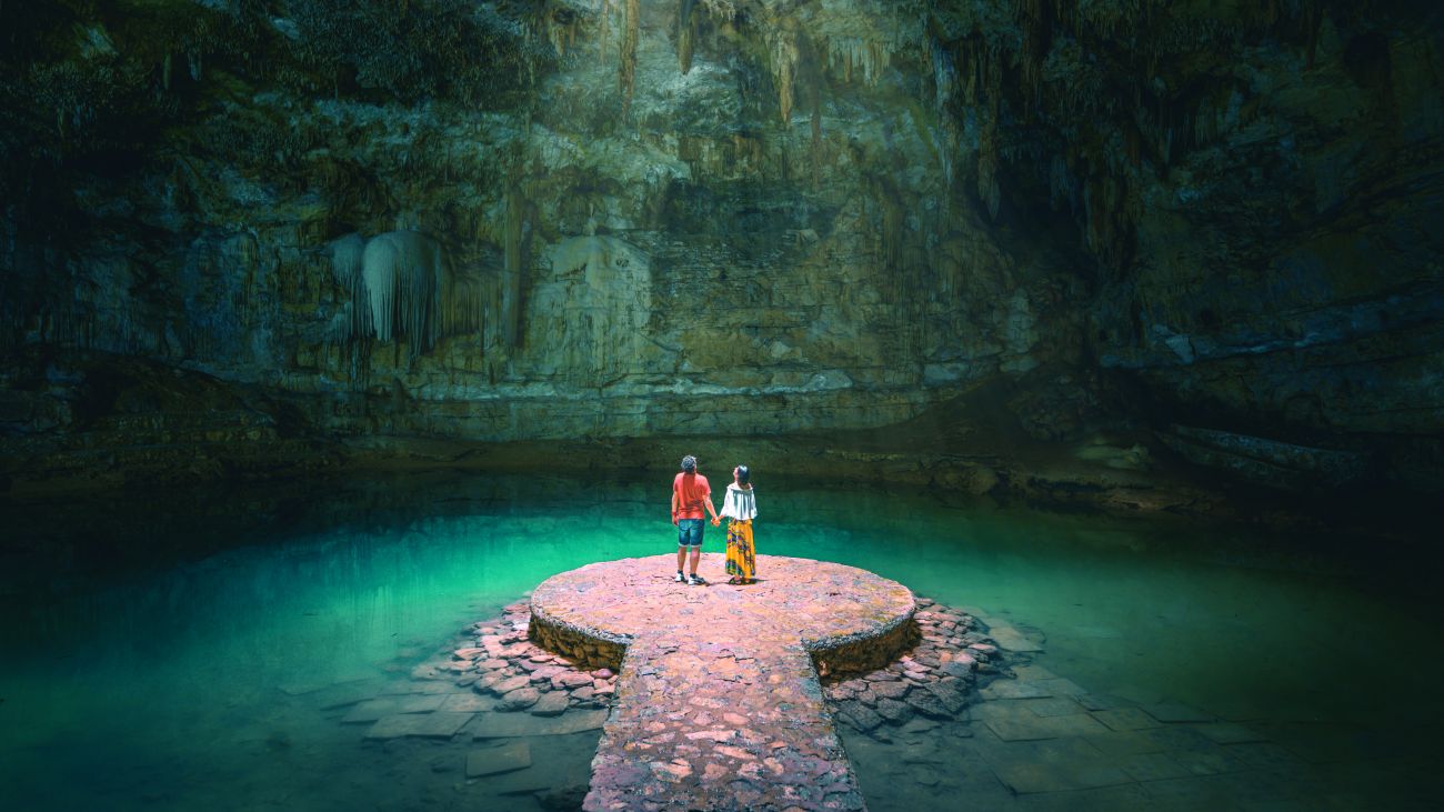 A couple standing on a stone platform in a tranquil cave with clear water.